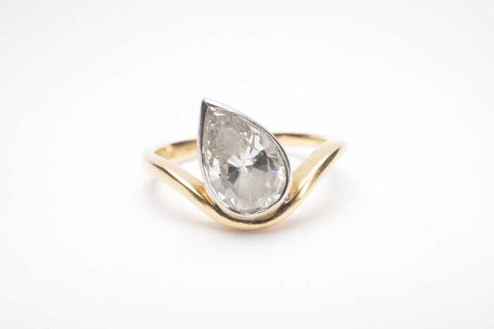 A bezel set pear cut diamond solitaire ring in 18ct yellow and white gold