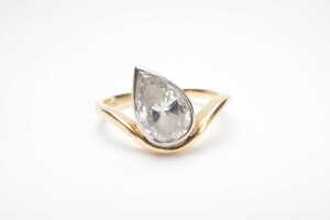 A bezel set pear cut diamond solitaire ring in 18ct yellow and white gold