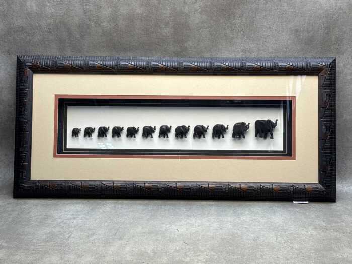 'The Migration, twelve graduated carved timber elephants in shadow box