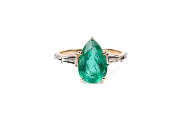 An emerald and diamond ring in 14 carat yellow gold