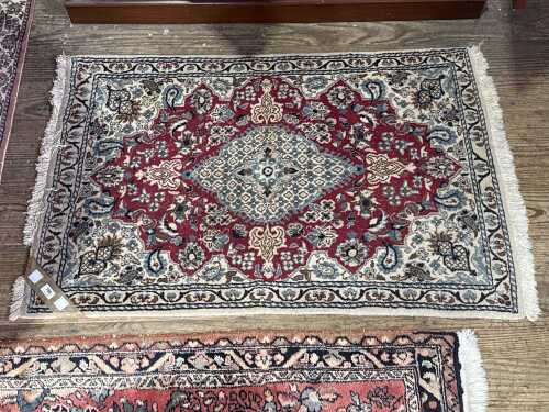 A Persian Mashad hand knotted wool rug in red and cream tones.