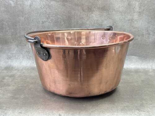 An antique copper pot with wrought iron handle