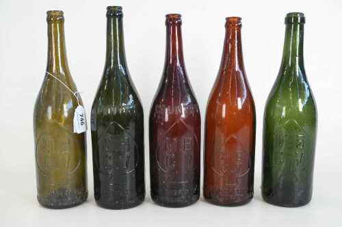 Five antique M.B.C.V. glass bottles in green and brown