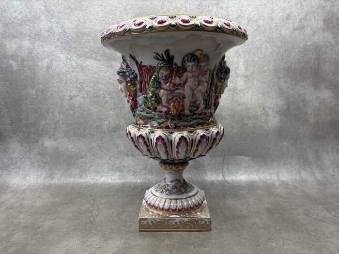 A Capodimonte Italian porcelain urn with hand painted relief scenes of puttis dancing and camping