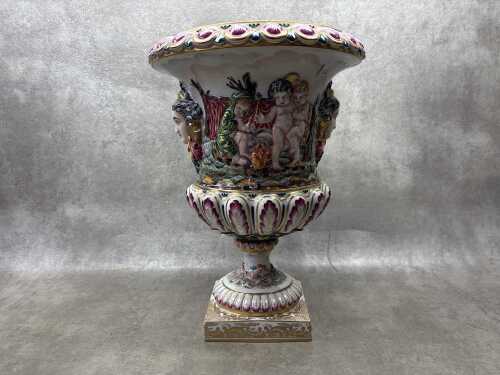 A Capodimonte Italian porcelain urn with hand painted relief scenes of puttis dancing and camping